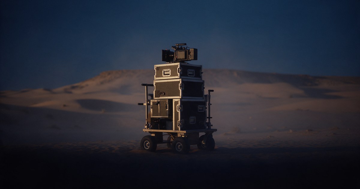 Equipment flight cases and a cinema camera on a cart at a desert location at dusk