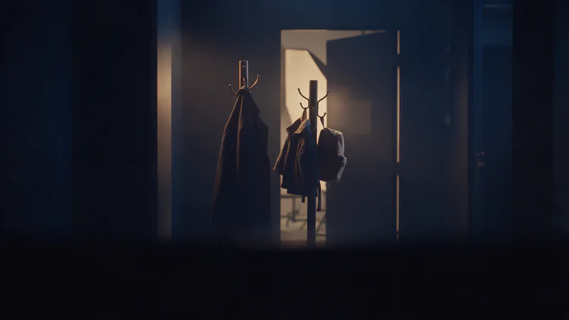 An adult coat beside a child-size jacket and backpack on coat stands at an open photo studio door