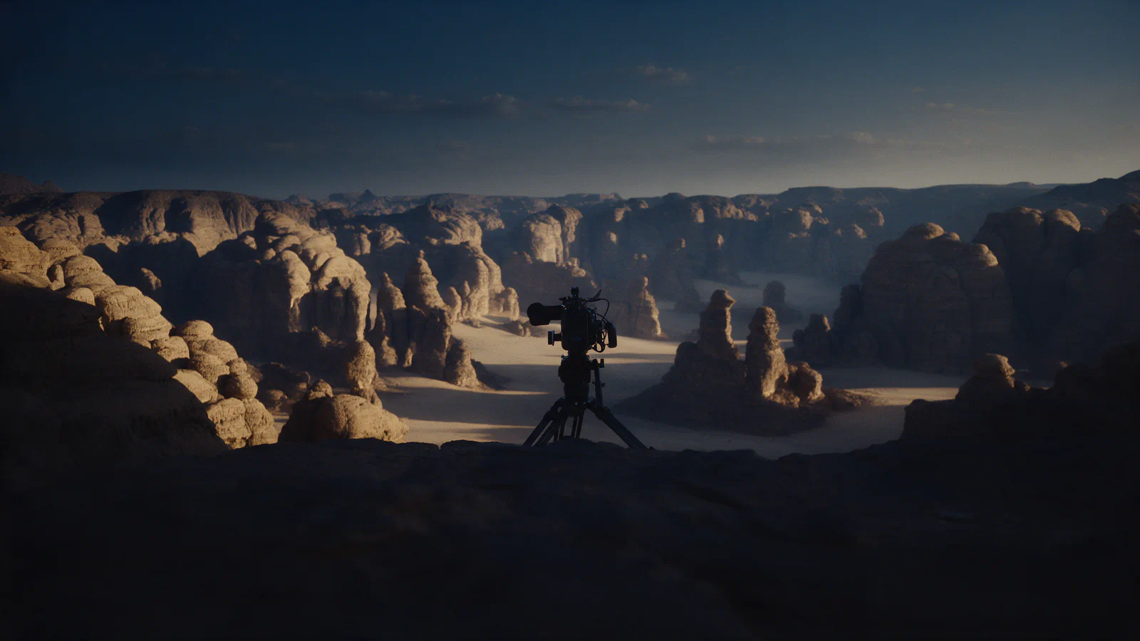 A cinema camera on a tripod overlooking a sandstone desert canyon at golden hour
